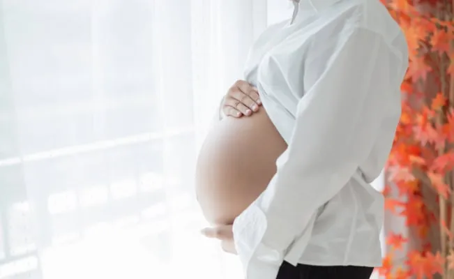Pregnant woman gently holding her belly near a window, symbolizing anticipation and comfort.