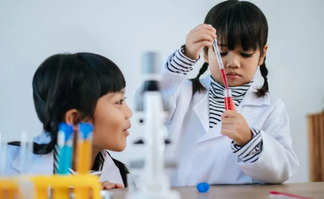 A woman lying in bed in a brightly lit room, appearing to be in pain or distress, with her eyes closed and hand grasping the bed sheet.