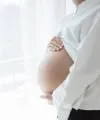 Pregnant woman gently holding her belly near a window, symbolizing anticipation and comfort.