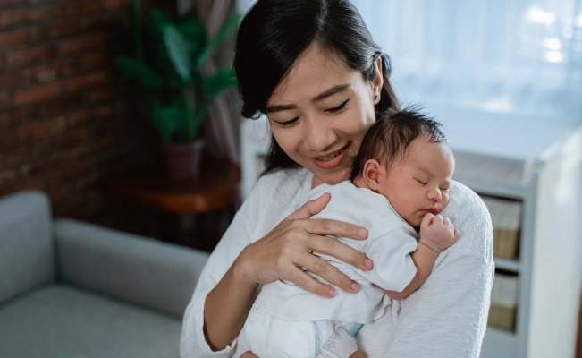 Full shot of mother holding newborn baby on bed.