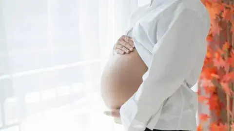 Pregnant woman gently holding her belly near a window, symbolizing anticipation and comfort.