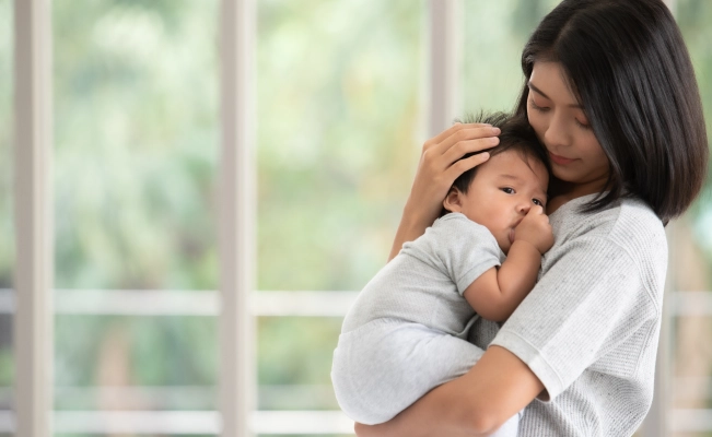 Mother cradling her baby with windows in the background.