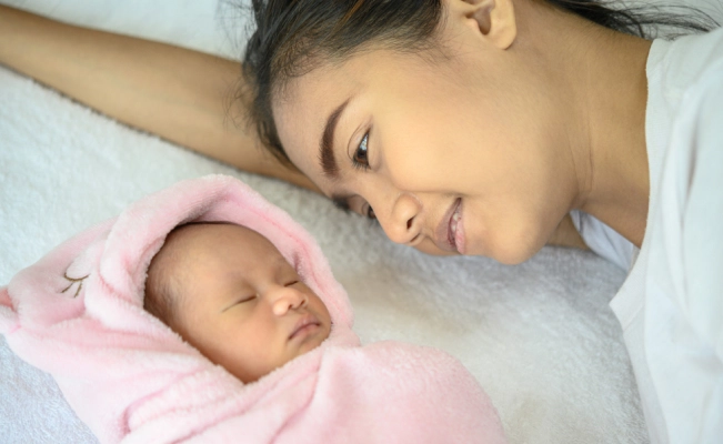 Mother lying on bed with newborn baby.